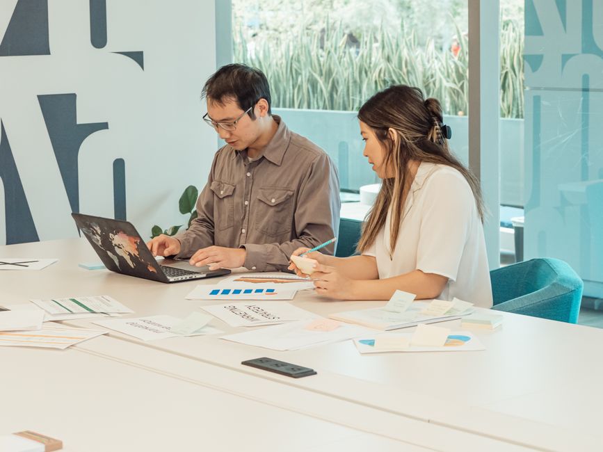 A real estate agent and a home seller having a professional discussion over documents at a modern dining table in a brightly lit home.