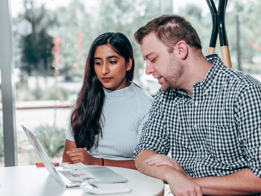 Two diverse professionals meeting at a bright, modern desk, collaborating over a laptop, representing a strategic partnership between a business owner and a digital agency.